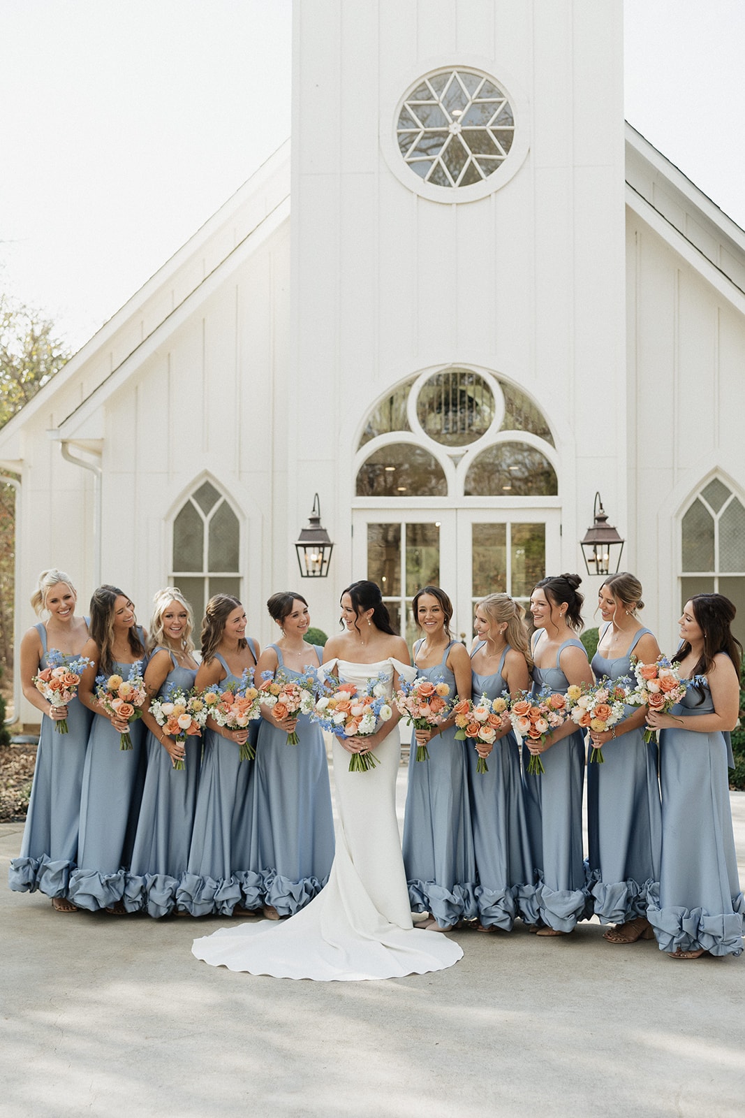 Avery with her bridesmaids in dusty blue ruffle dresses in front of the chapel