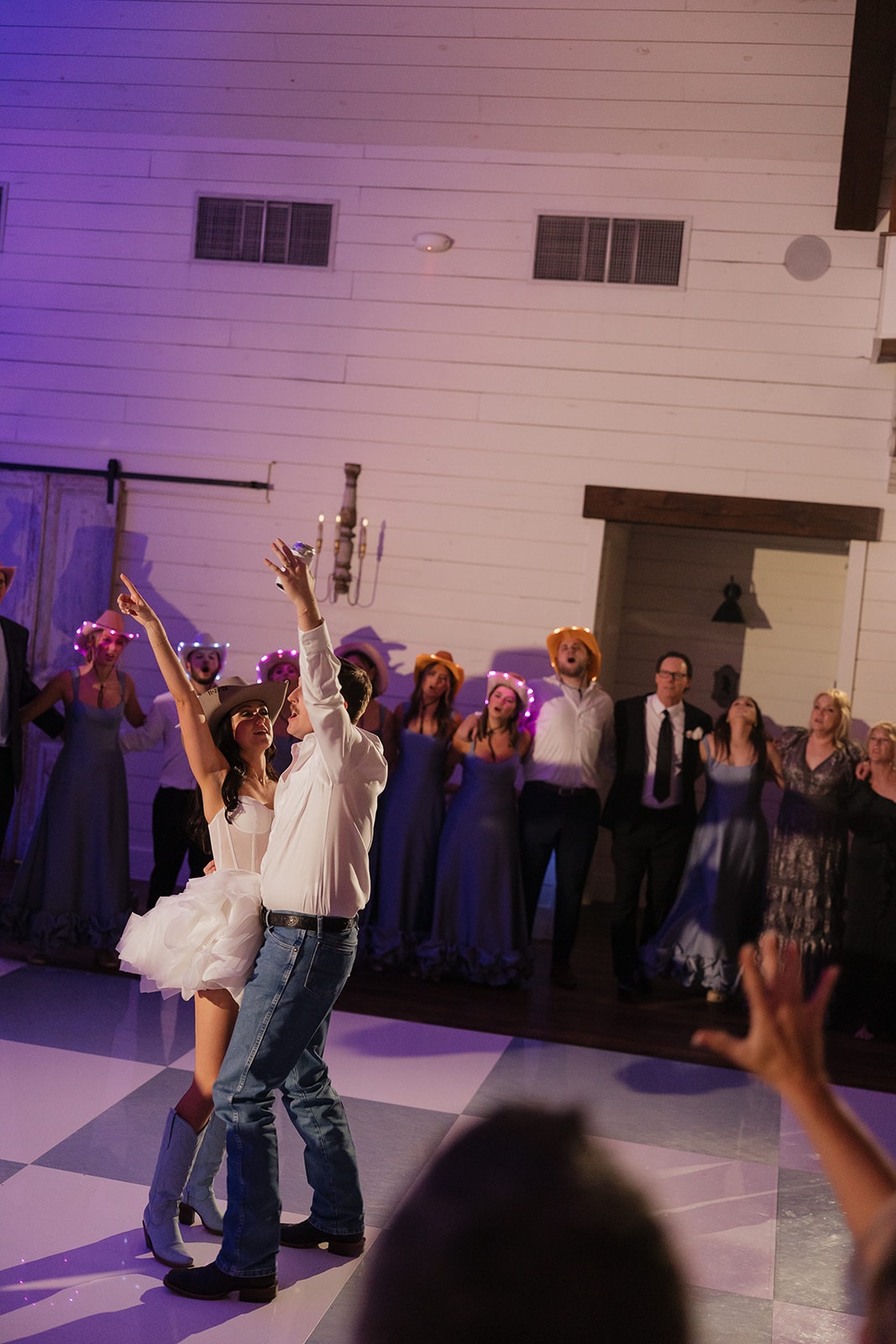 Avery and Pearson dancing on the checkered dance floor in cowboy hats with guests celebrating behind them