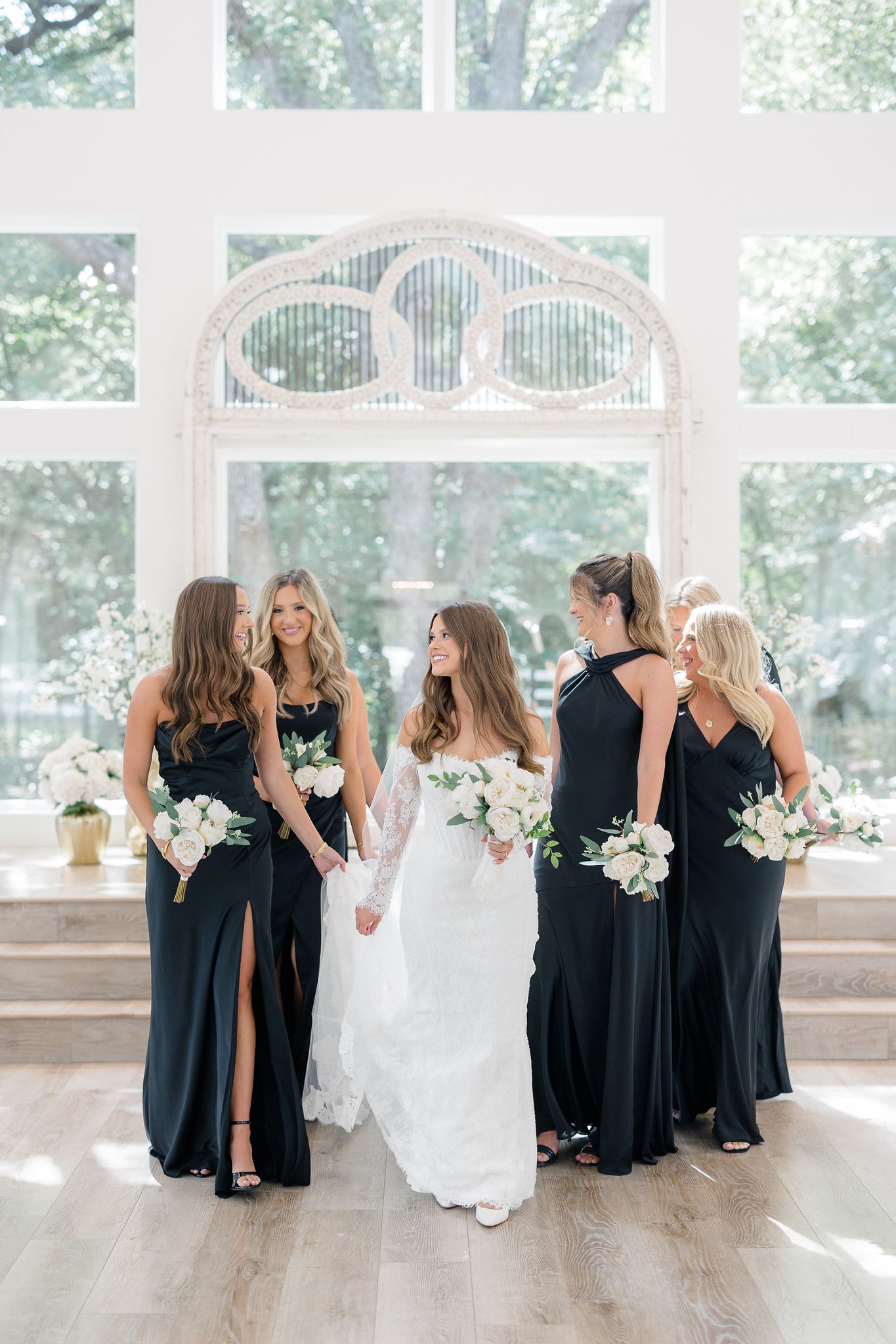 Catherine with her bridesmaids in black gowns holding white bouquets inside The French Farmhouse chapel