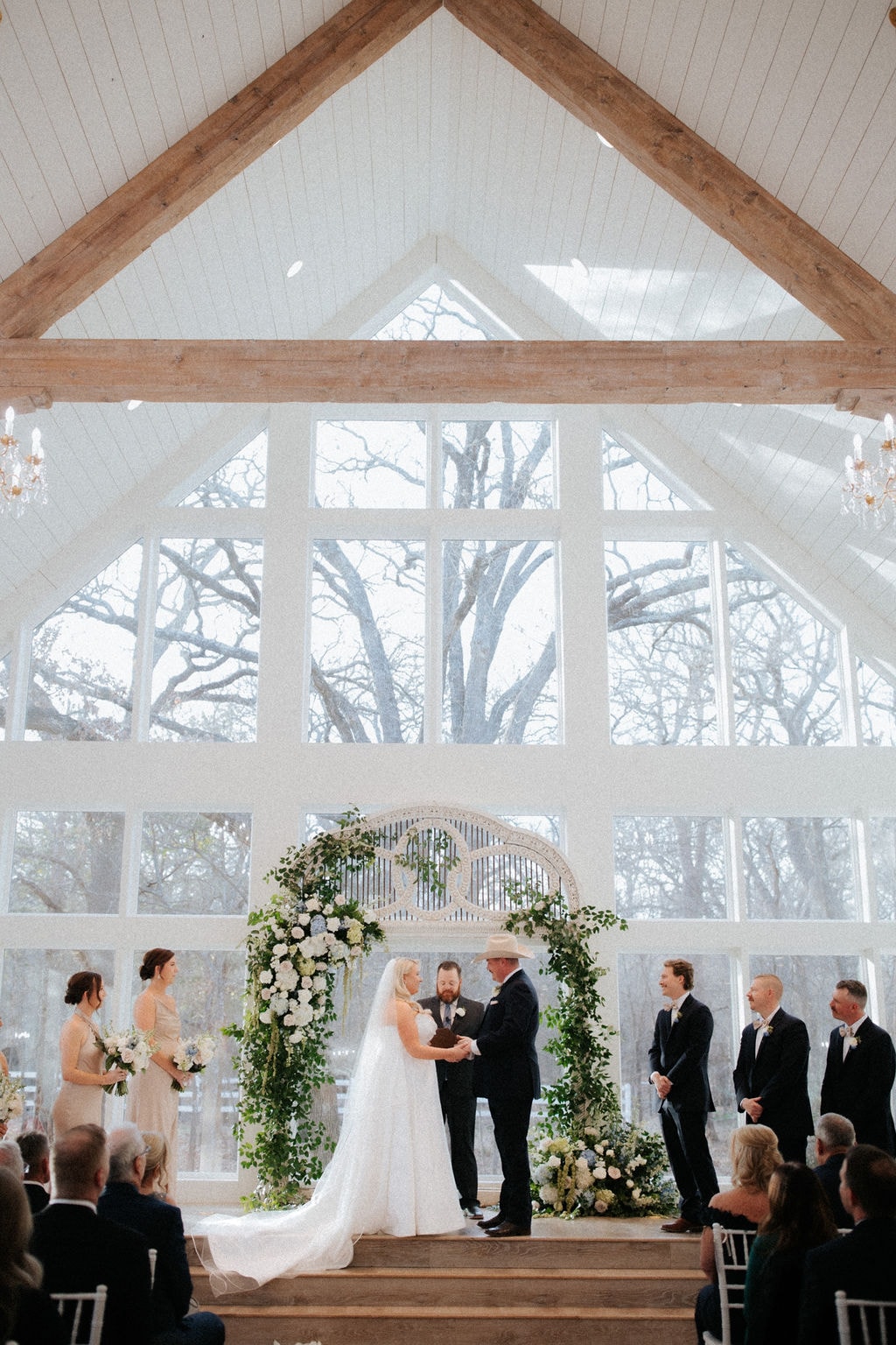 Kara and Anthony Marquardt exchanging vows inside The French Farmhouse chapel with a stunning white and green floral arch