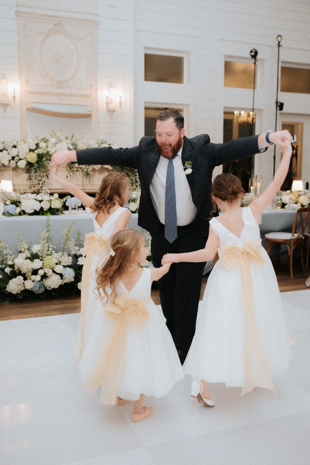 Anthony dancing with three flower girls in white dresses with gold sashes on the dance floor