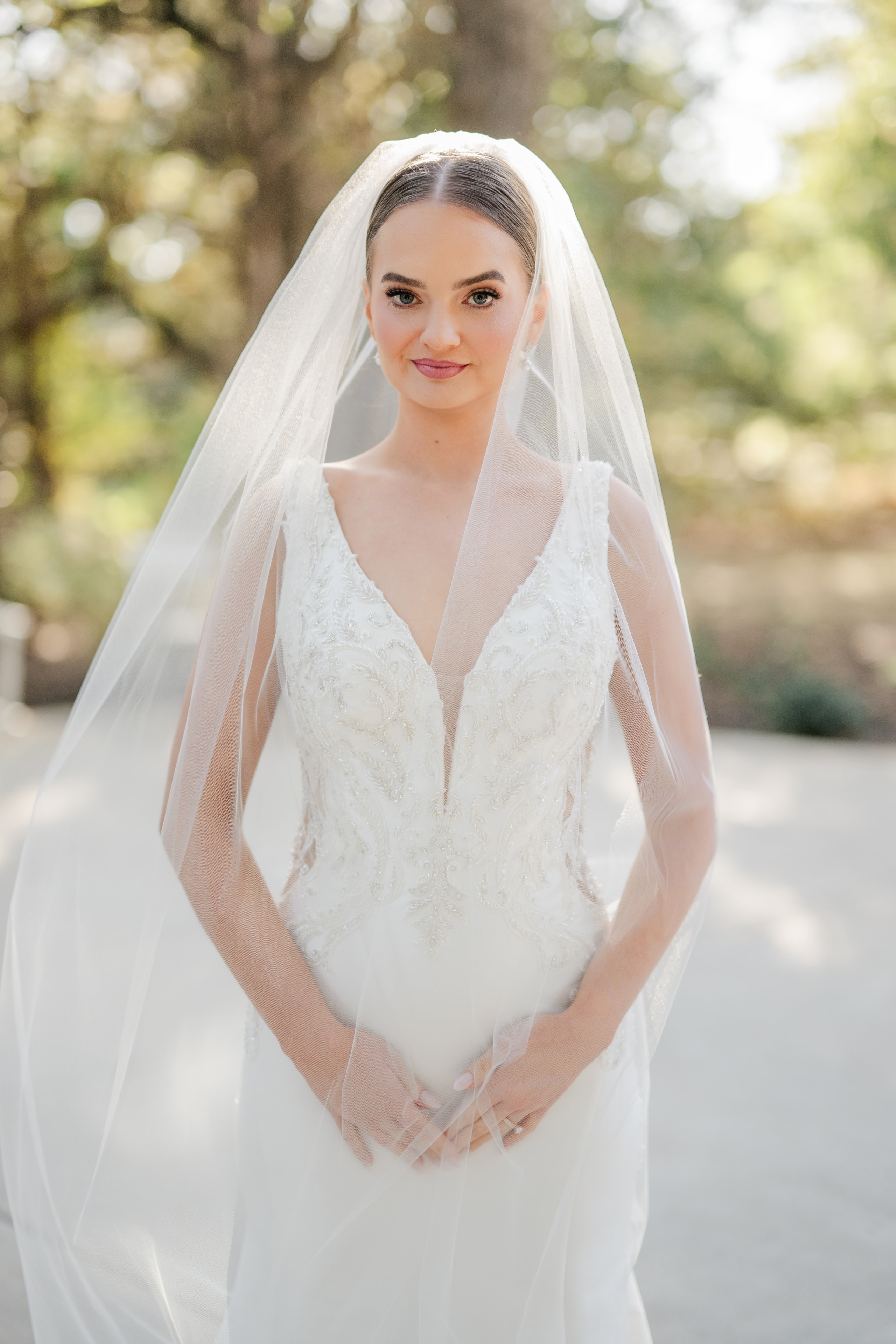 Bridal portrait outdoors on the grounds of The French Farmhouse Venue — bride in a beaded lace gown with cathedral veil, surrounded by lush oak trees