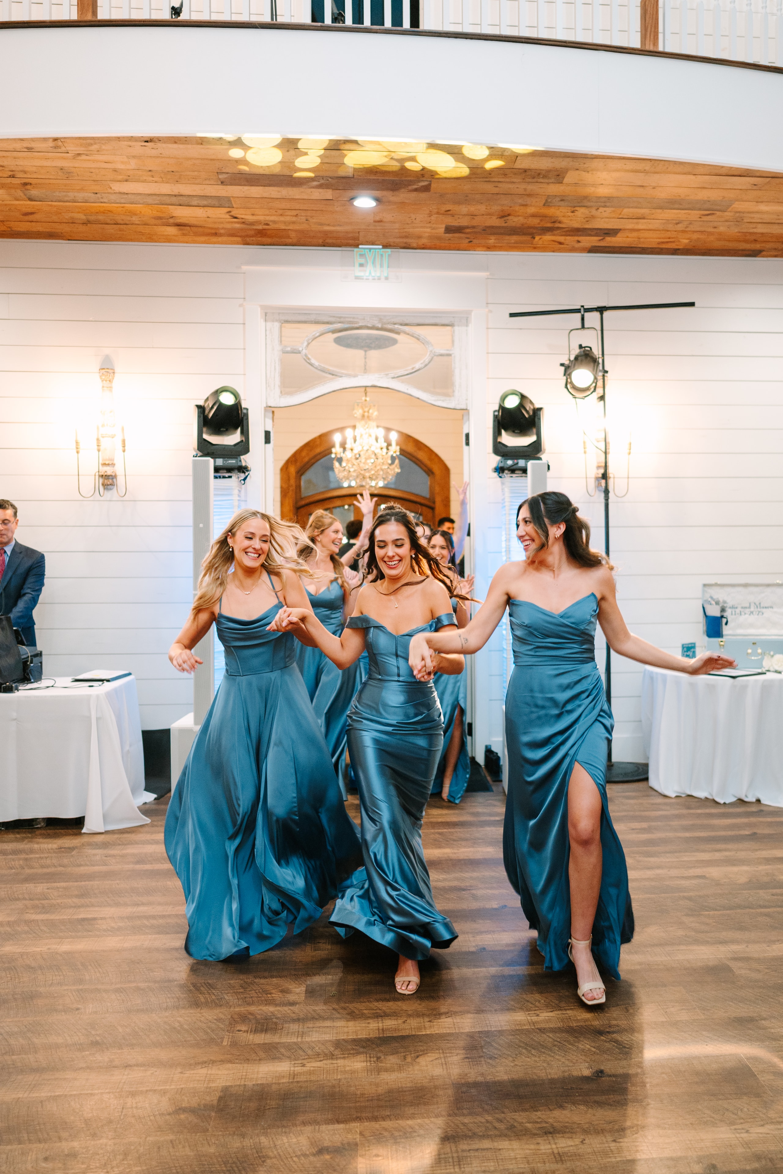 Katie's bridesmaids in steel blue satin gowns dancing and running into the reception hall at The French Farmhouse Venue during the grand entrance