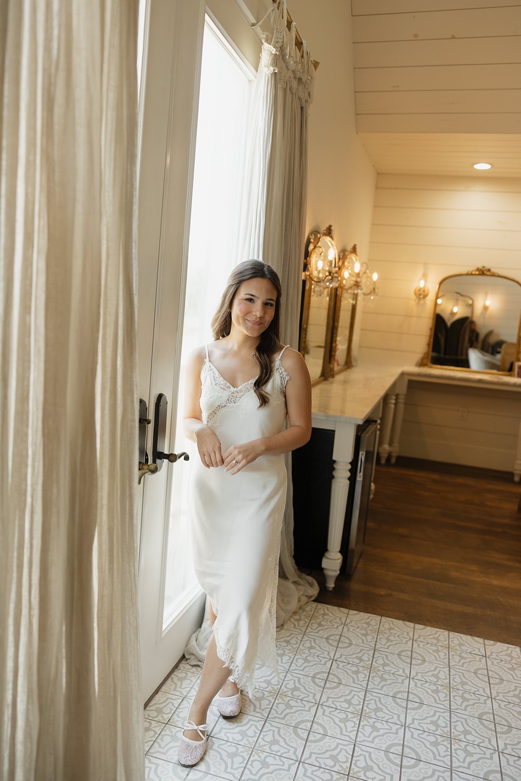 Nina standing in her slip dress by the French doors in the bridal suite at The French Farmhouse Venue on the morning of her 4th of July wedding