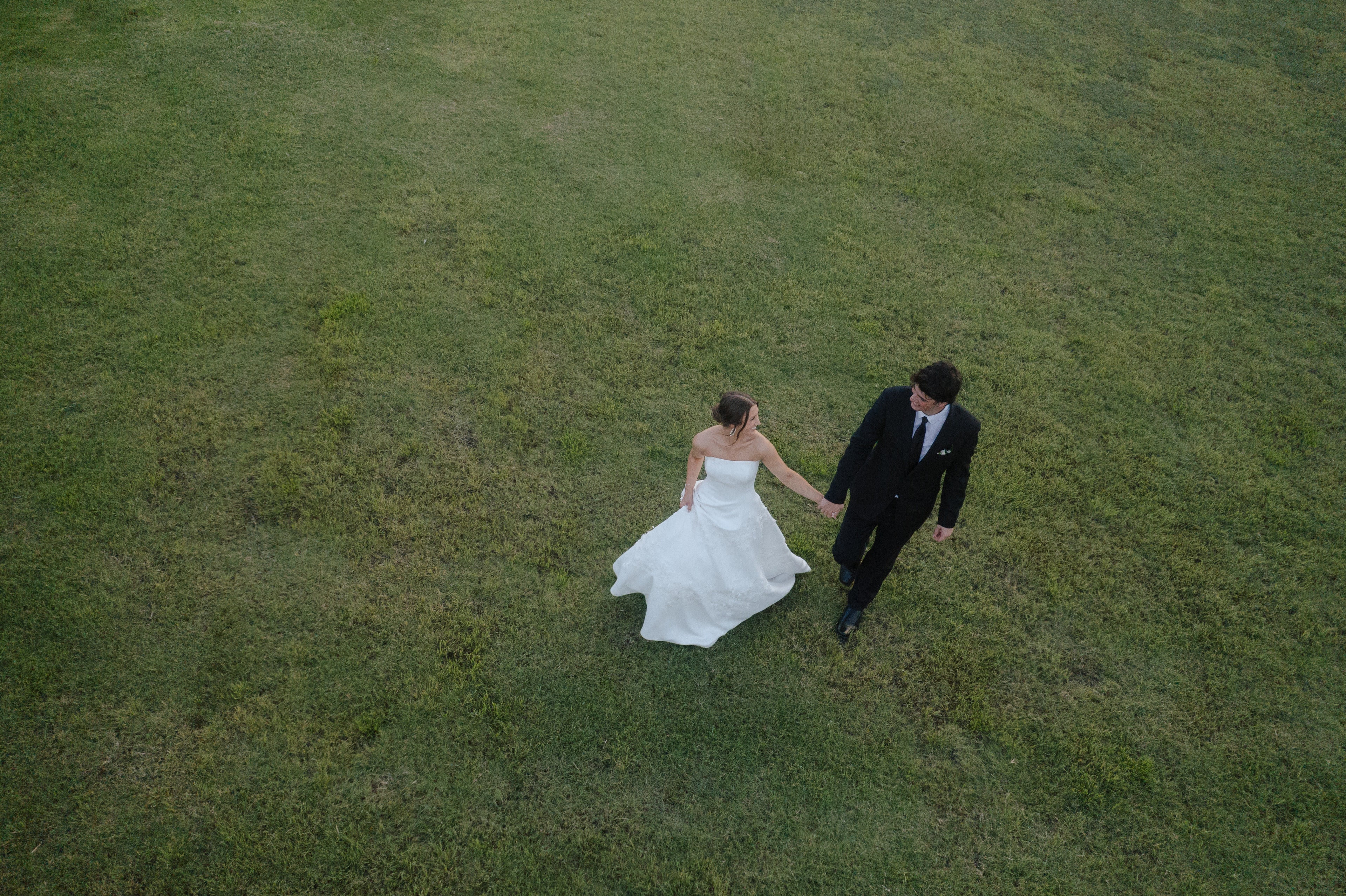 Aerial drone photo of Paige and DJ lying in the grass kissing on the grounds of The French Farmhouse Venue
