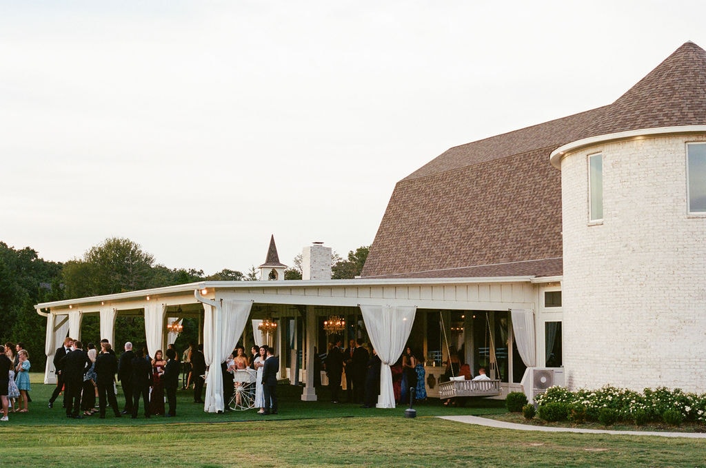 Guests enjoying cocktail hour under the 30-foot covered pavilion with curtains and chandeliers at The French Farmhouse Venue