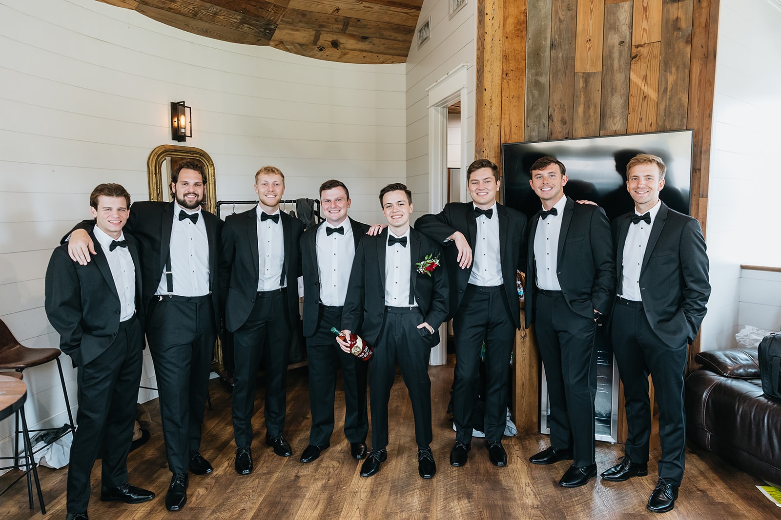 Groom and groomsmen in matching black tuxedos posing together in the Groom's Room